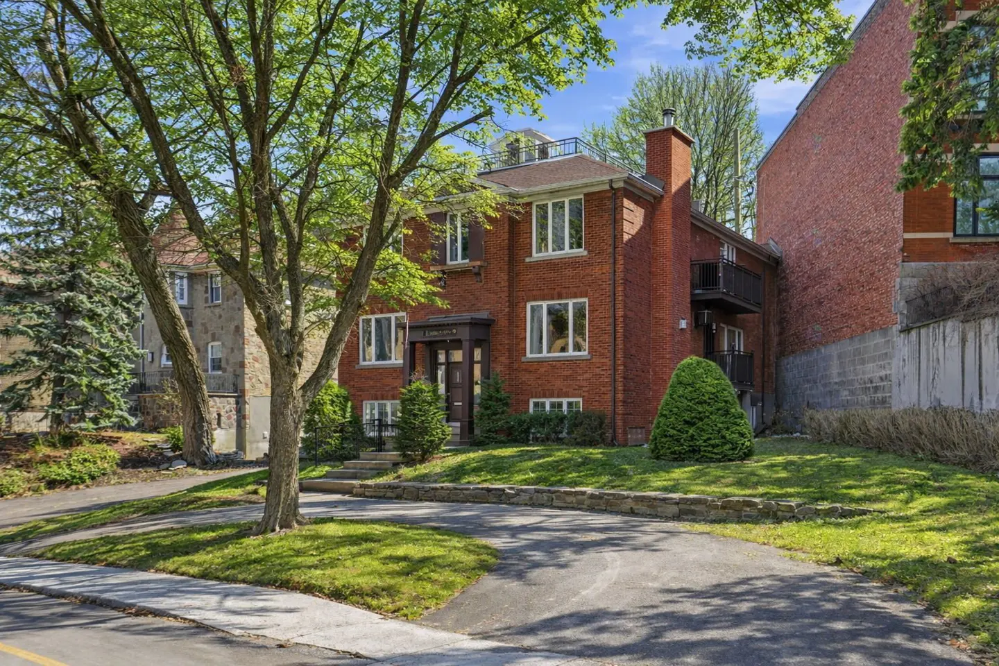 A two-story red brick building with white-framed windows and a dark brown door is surrounded by green trees and grass.