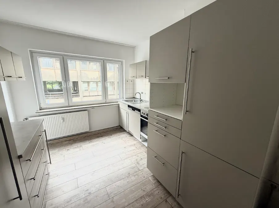 Bright kitchen with white cabinets, stainless steel handles, and wood floors. A large window provides natural light.