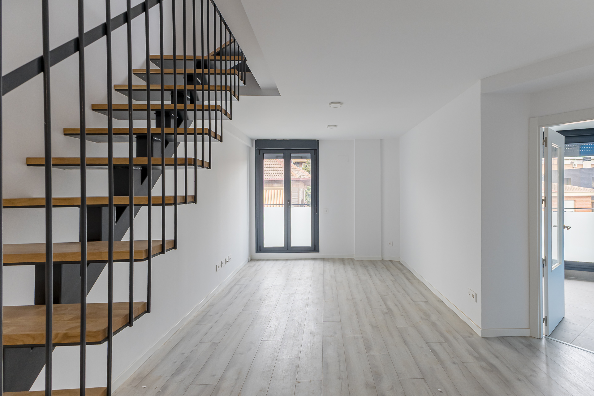 Modern living room with light wood floors, white walls, and a floating staircase with wooden steps and black metal railings. [AI-generated text]