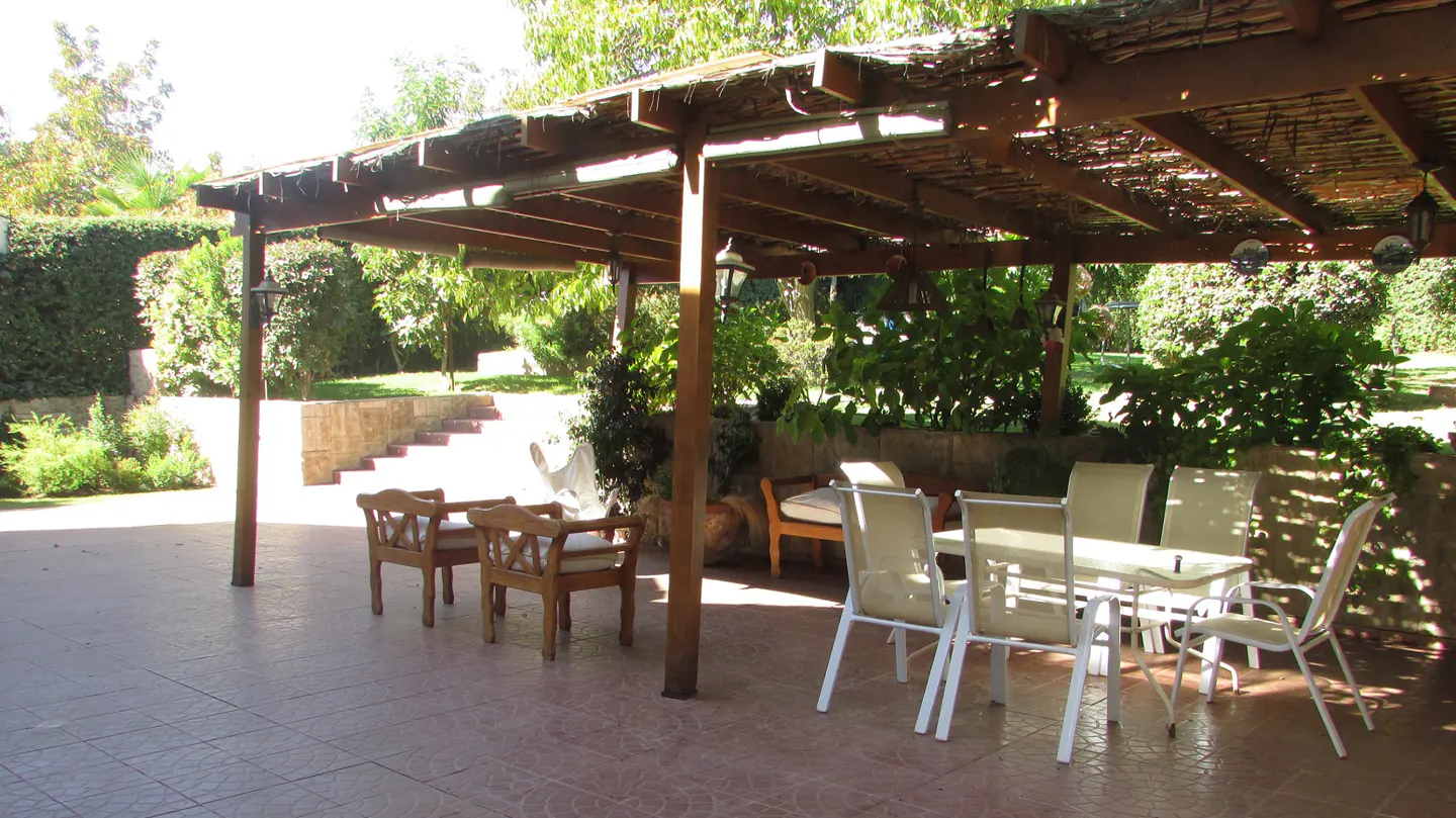 Outdoor patio with a wooden pergola, table, chairs, and lush greenery.
