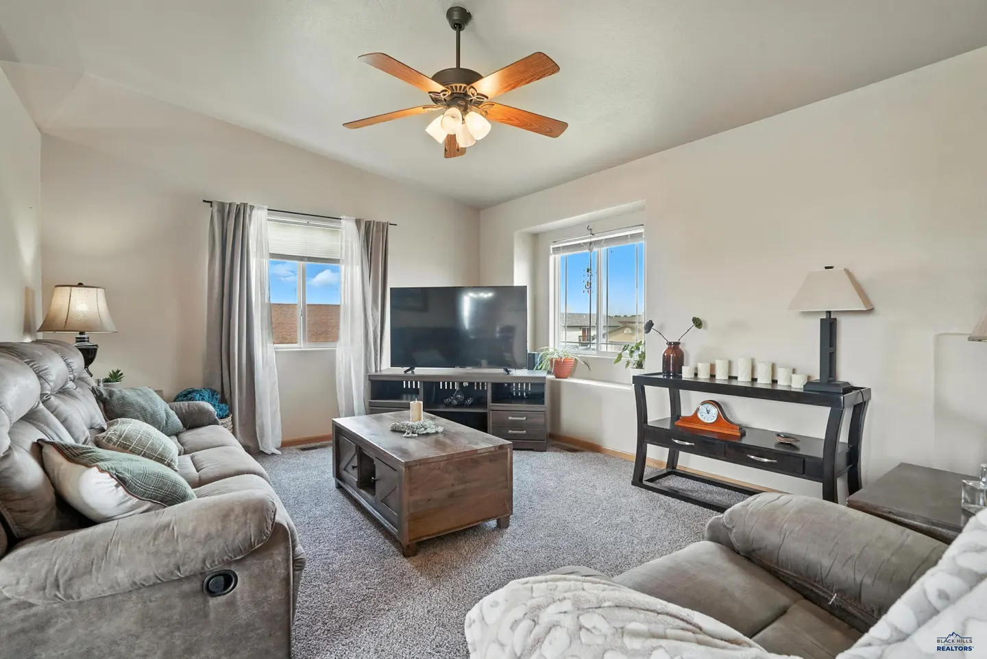 Living room with gray carpet, a brown sectional sofa, wooden coffee table, TV stand, and a console table with lamps.