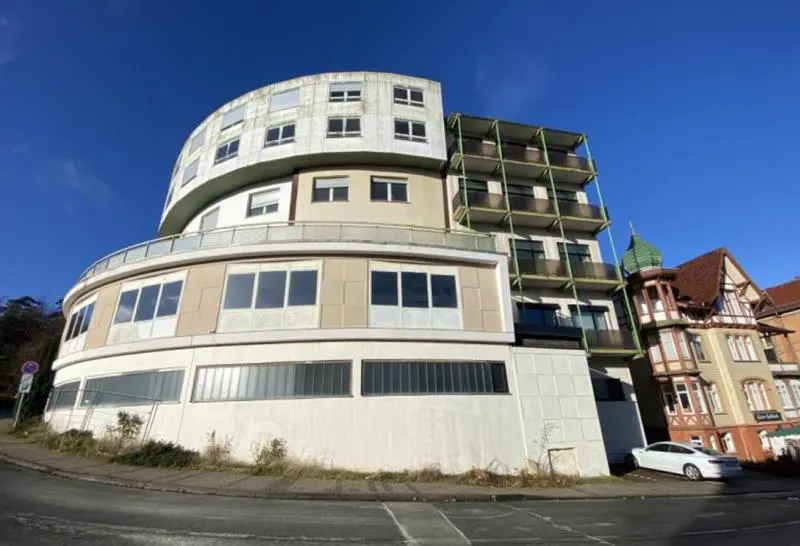 Exterior view of a multi-story, curved building with balconies, next to a traditional building under a clear blue sky.