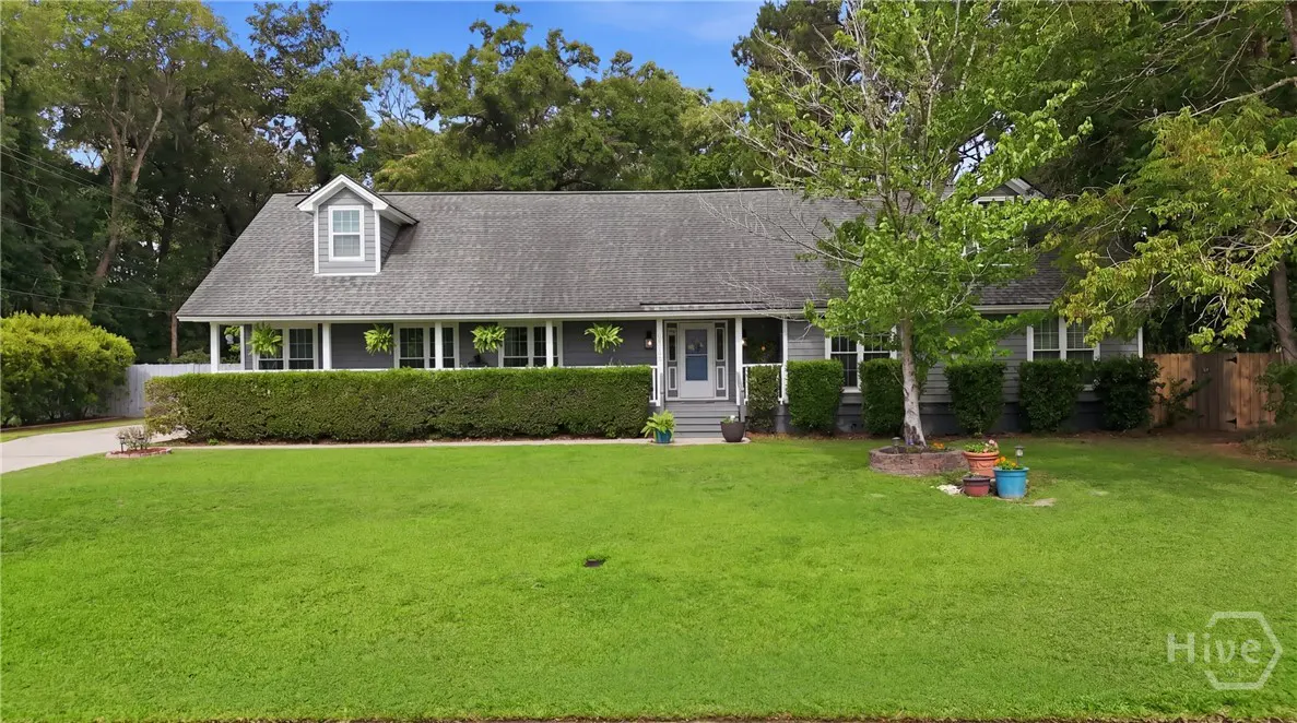 A gray single-story house with a gray roof, white trim, and a large green lawn. A trimmed hedge runs along the front of the house.