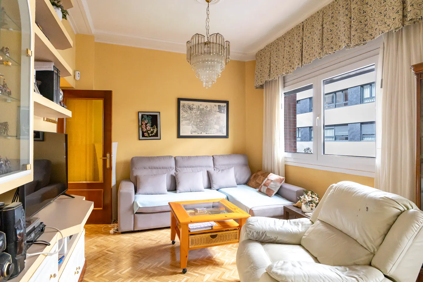 Living room with yellow walls, a gray sectional sofa, a wooden coffee table, and a white armchair near a window.