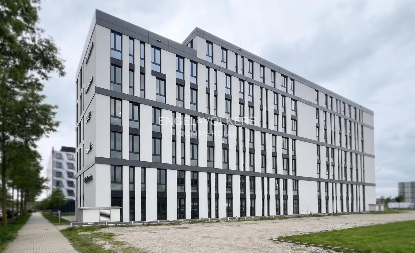 Exterior view of a modern, multi-story commercial building with white and gray facade, and many windows. Engel & Volkers logo is visible.