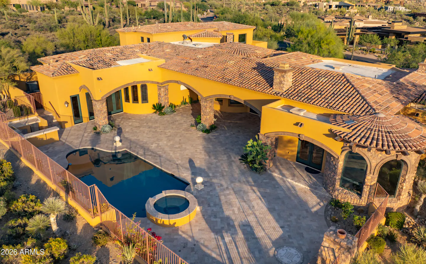 Aerial view of a yellow stucco home with a red tile roof, pool, spa, and desert landscaping.