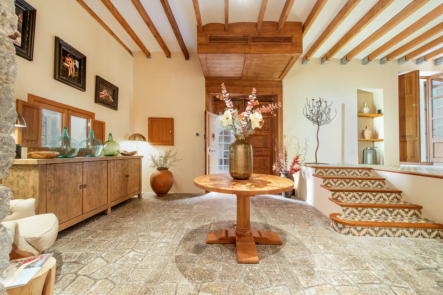 Interior view of a home's foyer with stone floors, wood beams, and a round table with a vase of flowers.