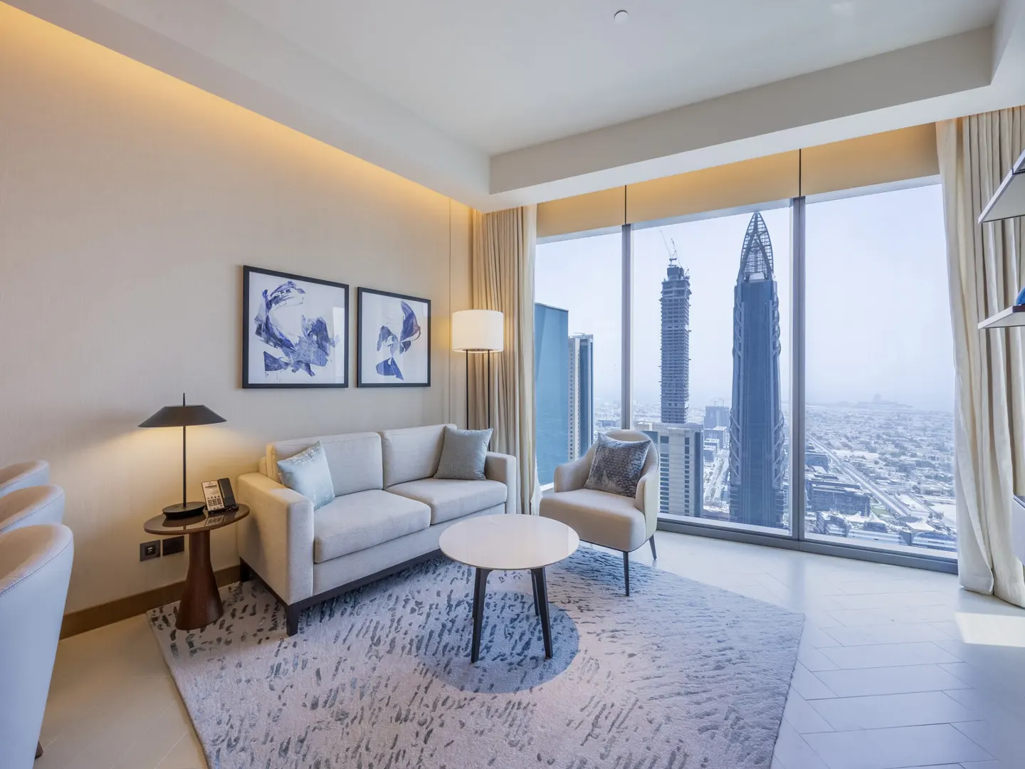 Modern living room with beige sofa, armchair, and coffee table, featuring floor-to-ceiling windows with city skyline views.