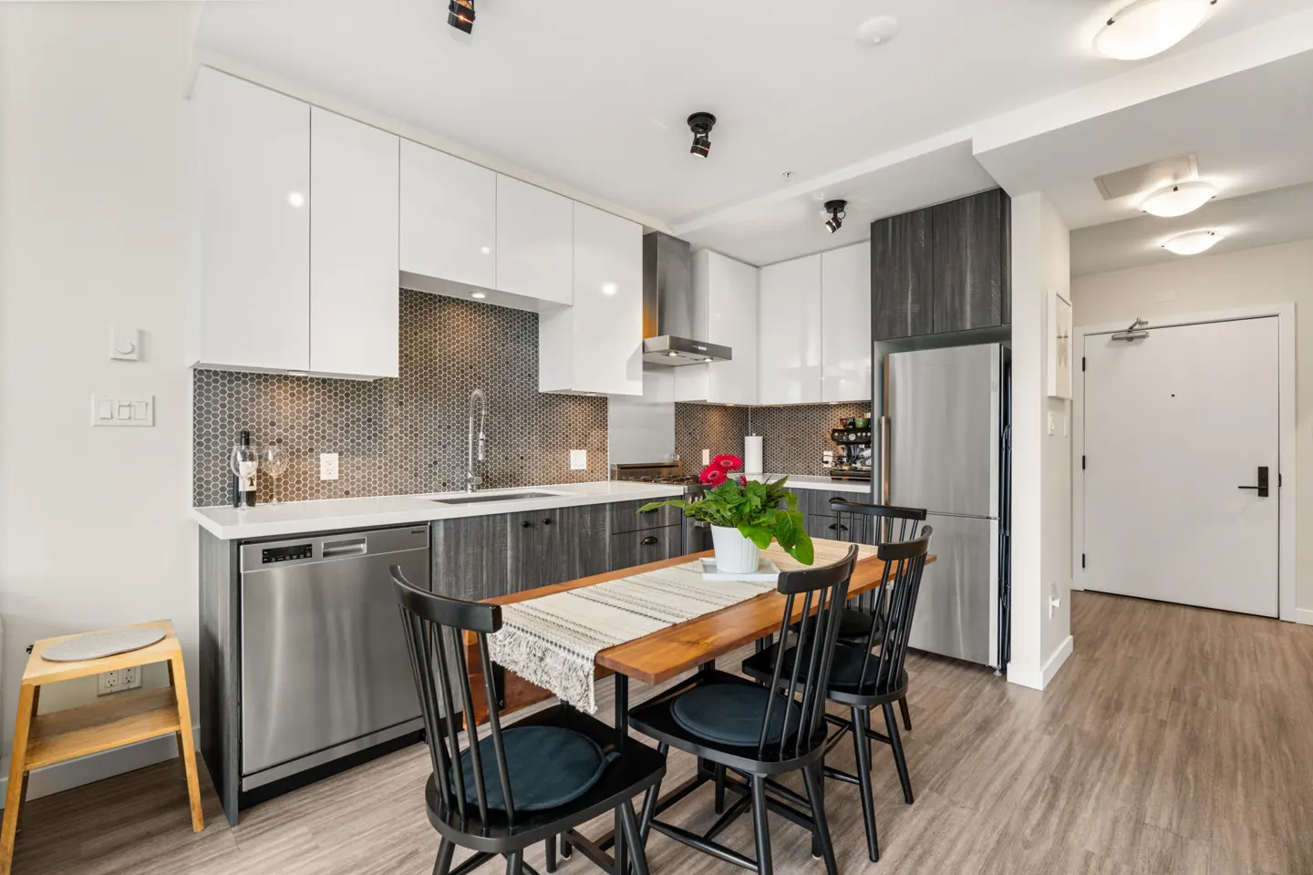 A modern kitchen with white and gray cabinets, stainless steel appliances, and a wooden dining table with black chairs.