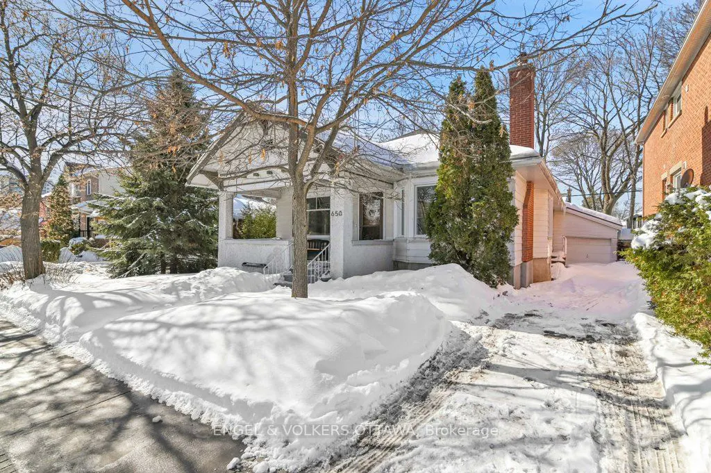 A white bungalow with a front porch is surrounded by snow on a sunny winter day.