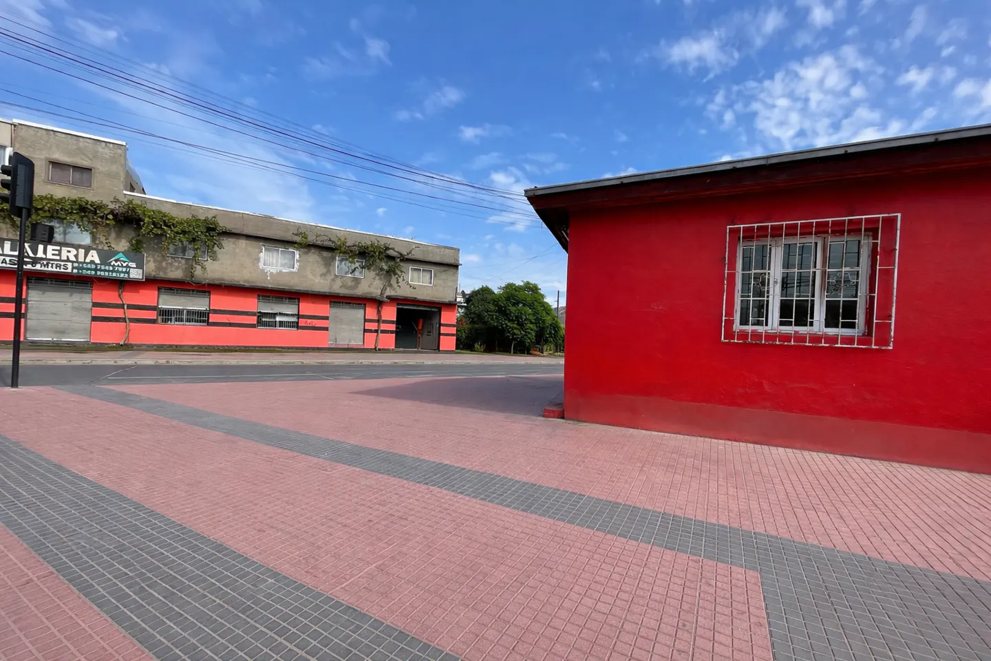 Street view of a red building with a barred window, and a gray building with a red stripe, under a blue sky.