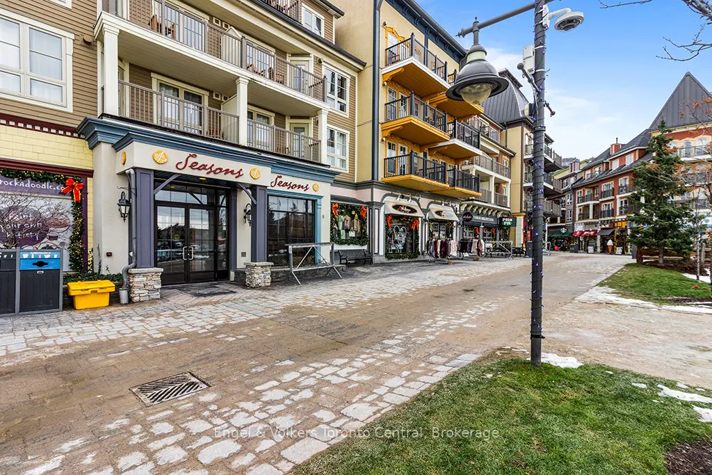 Outdoor view of a cobblestone street lined with shops and restaurants in a village setting. Balconies adorn the upper levels of the buildings.