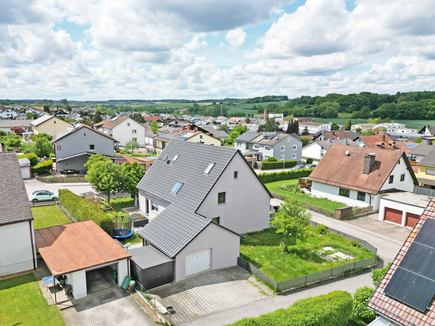 Aerial view of a modern grey house with a dark roof, a detached garage, and a green yard in a quiet suburban neighborhood.