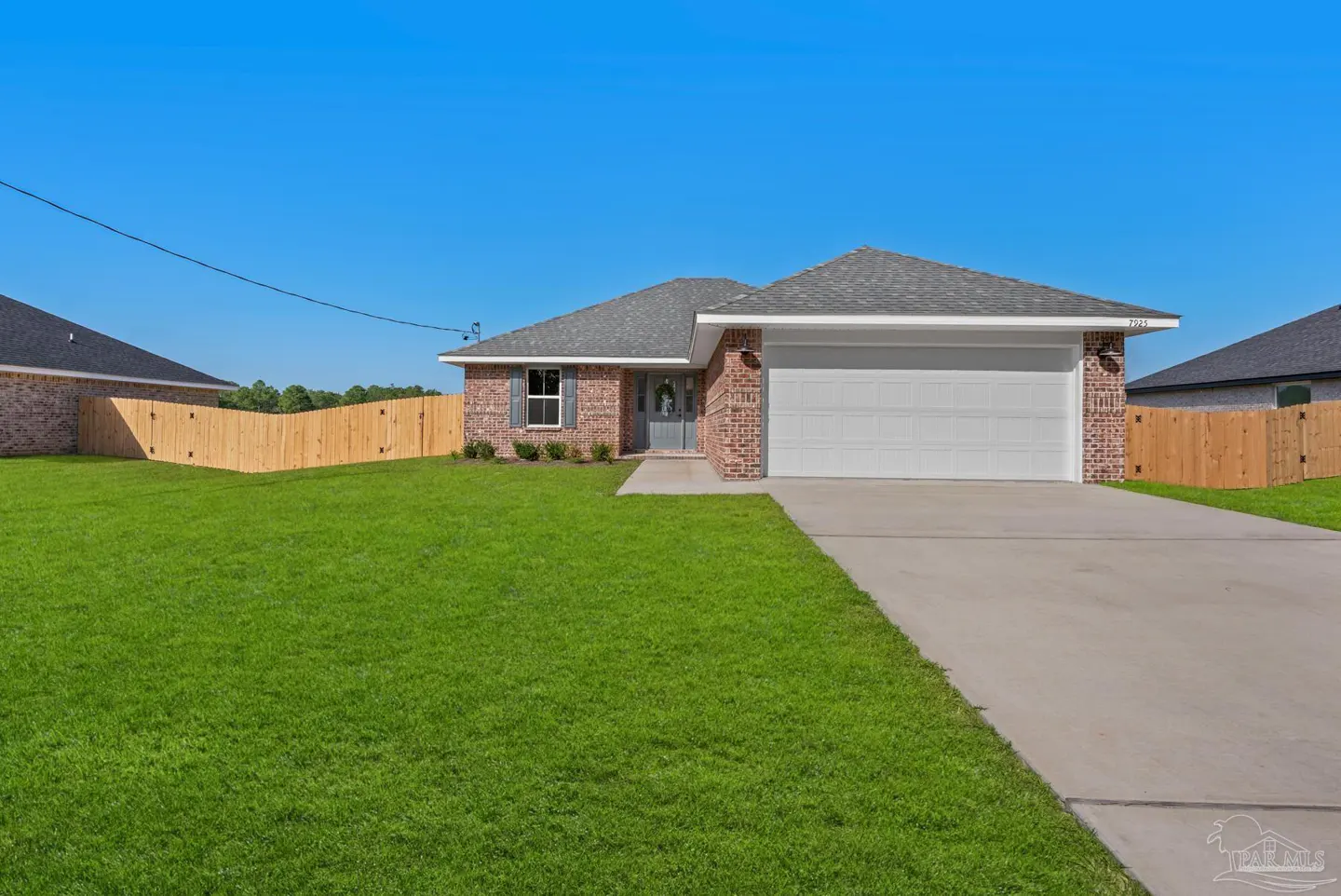 A single-story brick house with a gray roof, white garage door, and green lawn under a blue sky.