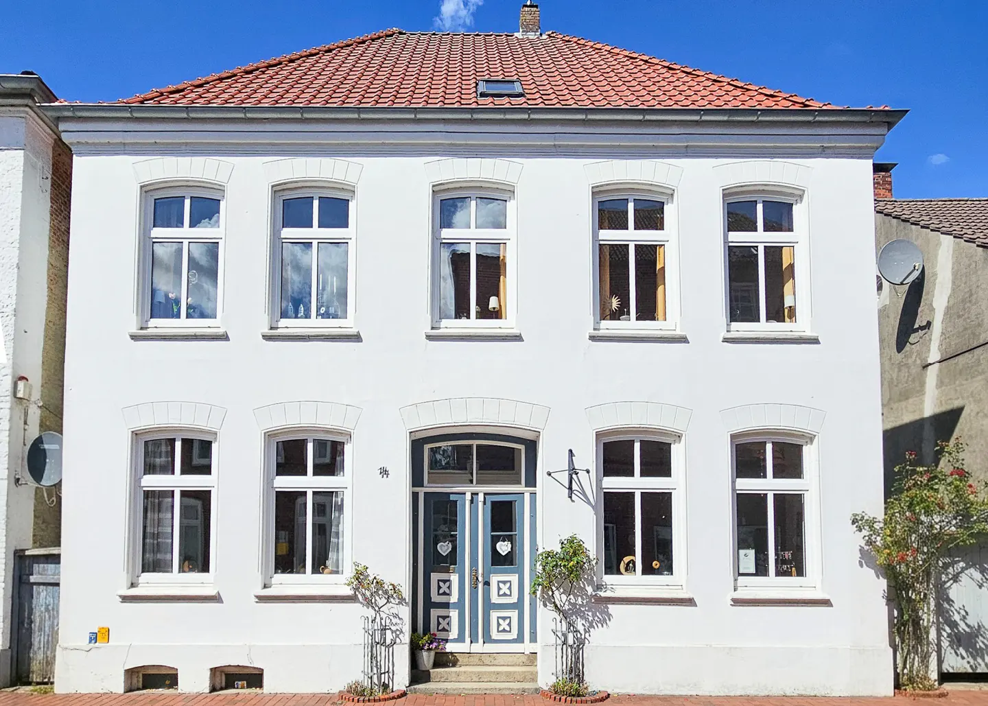 Two-story white house with a red tile roof and blue and white doors under a bright blue sky.