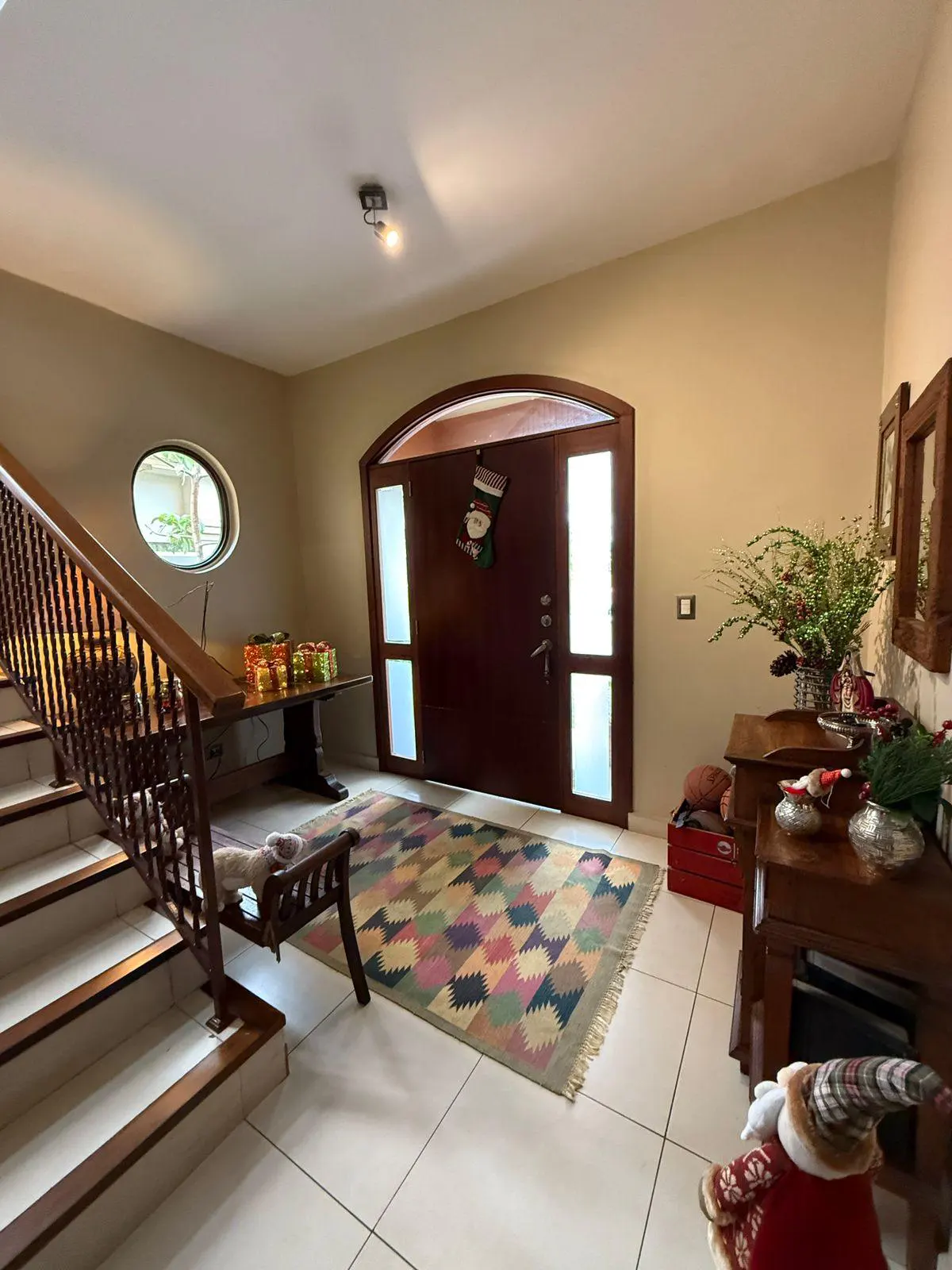 Foyer with stairs, a dark wood door with a stocking, and a colorful rug on white tile. Christmas decorations are visible.