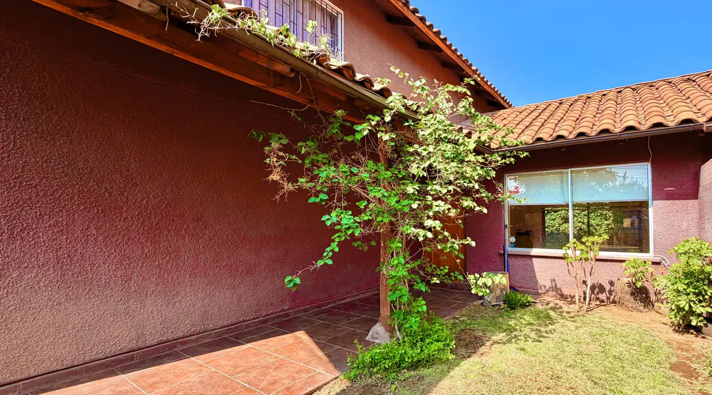 Exterior of a red-brown house with a red tile roof, a green vine, and a small lawn.