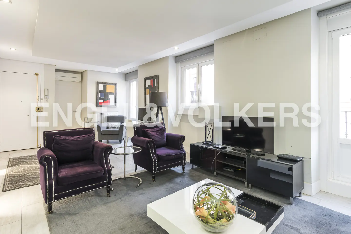 A living room with two purple armchairs, a white coffee table, and a black TV stand. There is a gray rug on the floor.