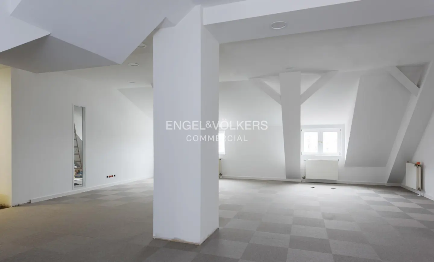 Bright, empty commercial space with white walls, gray checkered floors, and support beams. Engel & Volkers logo on a column.