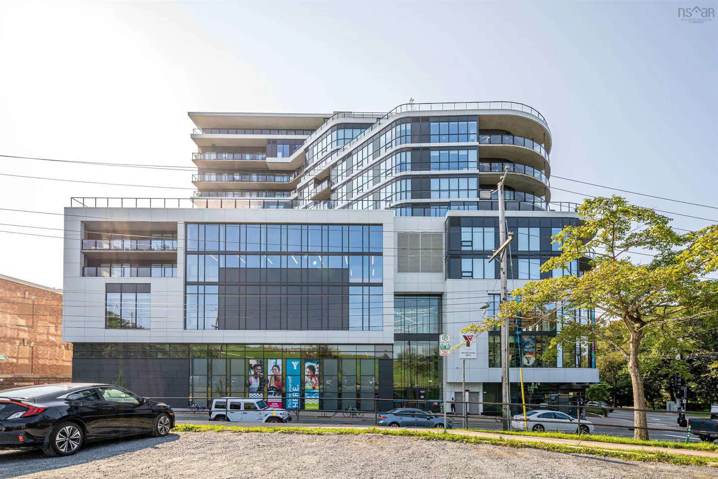 Modern mixed-use building with a YMCA on the lower floors and condos above. Cars parked in front.