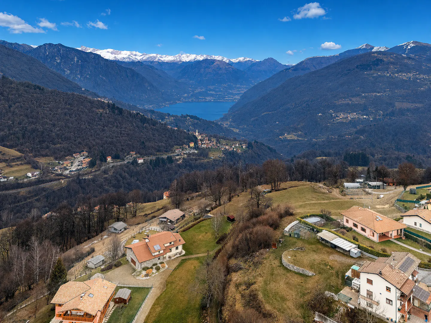 Scenic view of houses on a hillside, with mountains, a lake, and a blue sky in the background.