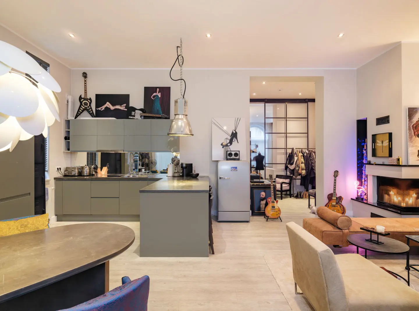 Open-concept living space with a gray kitchen, island, guitars, and a fireplace. The floor is light wood.