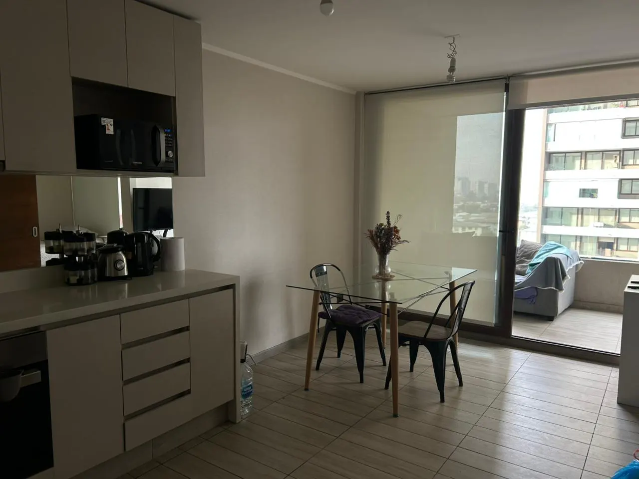 Apartment interior with a kitchen counter, glass table with chairs, and a balcony with city views.