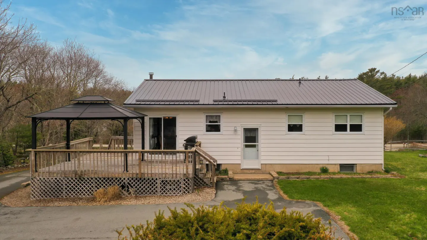 Back of a white house with a metal roof, deck, and gazebo on a sunny day.