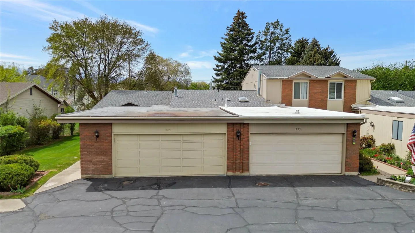 Two-car garage with brick accents and beige doors, numbers 333 and 335, on a cracked asphalt driveway. Trees and blue sky in background.