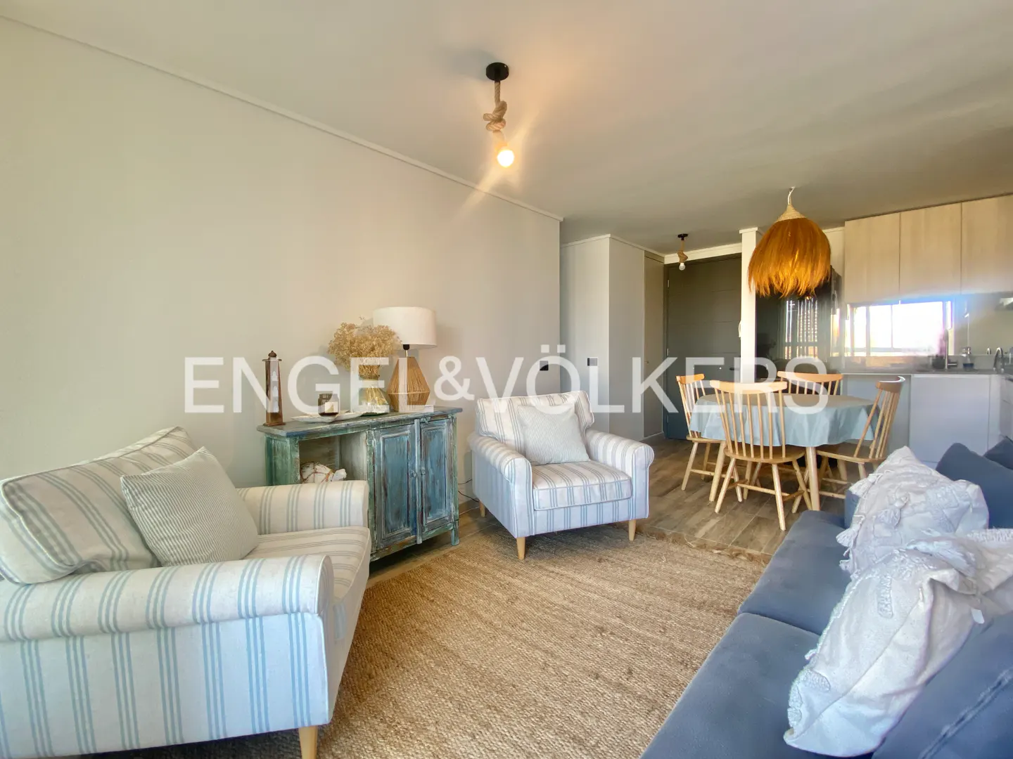 Living room with blue striped armchairs, a blue sofa, a round table with wooden chairs, and a blue distressed cabinet.