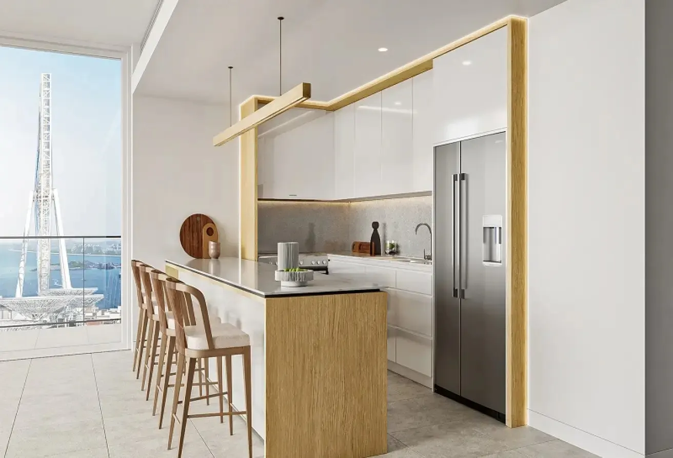 A modern kitchen with white cabinets, a stainless steel refrigerator, and a wooden breakfast bar with stools. A large window overlooks a waterfront view.