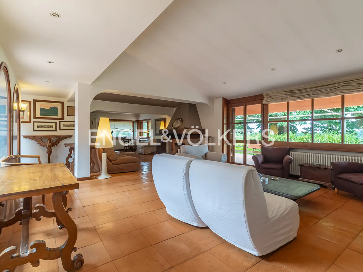 Spacious living room with terracotta tile floor, white sofas, and large windows overlooking greenery.