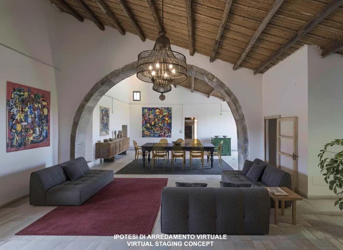 Bright, airy living room with stone archway, wood-beamed ceiling, and modern gray sofas. A large chandelier hangs above a dining table. Colorful art adorns the walls.