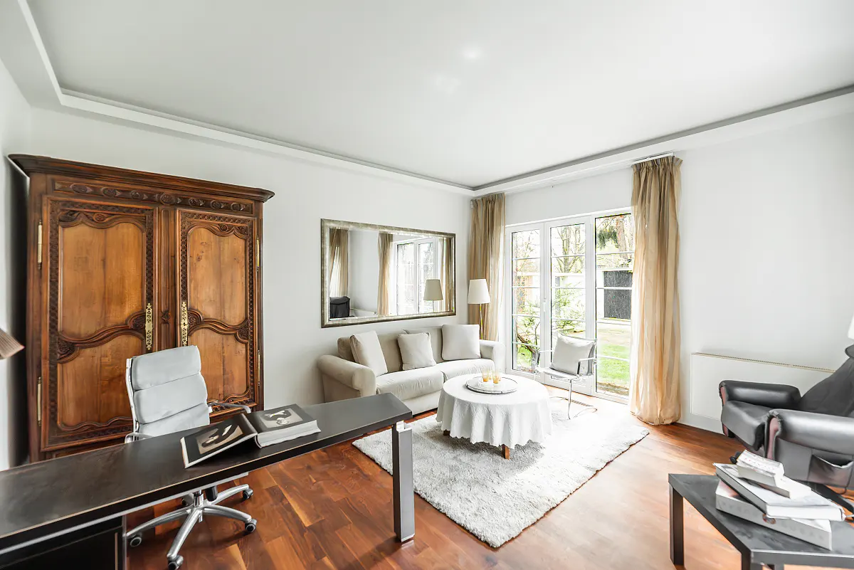 Bright living room with hardwood floors, a desk, a sofa, and a large wooden armoire. Natural light streams in through the windows.