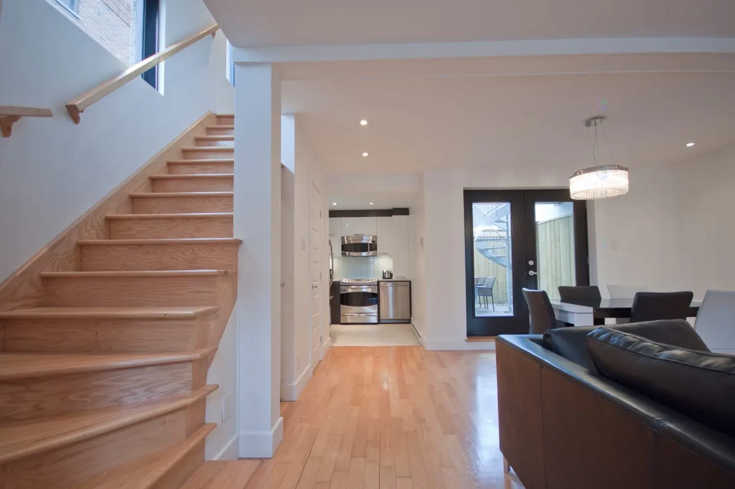 Open-concept living area with hardwood stairs, a modern kitchen, dining space, and a black leather sofa.