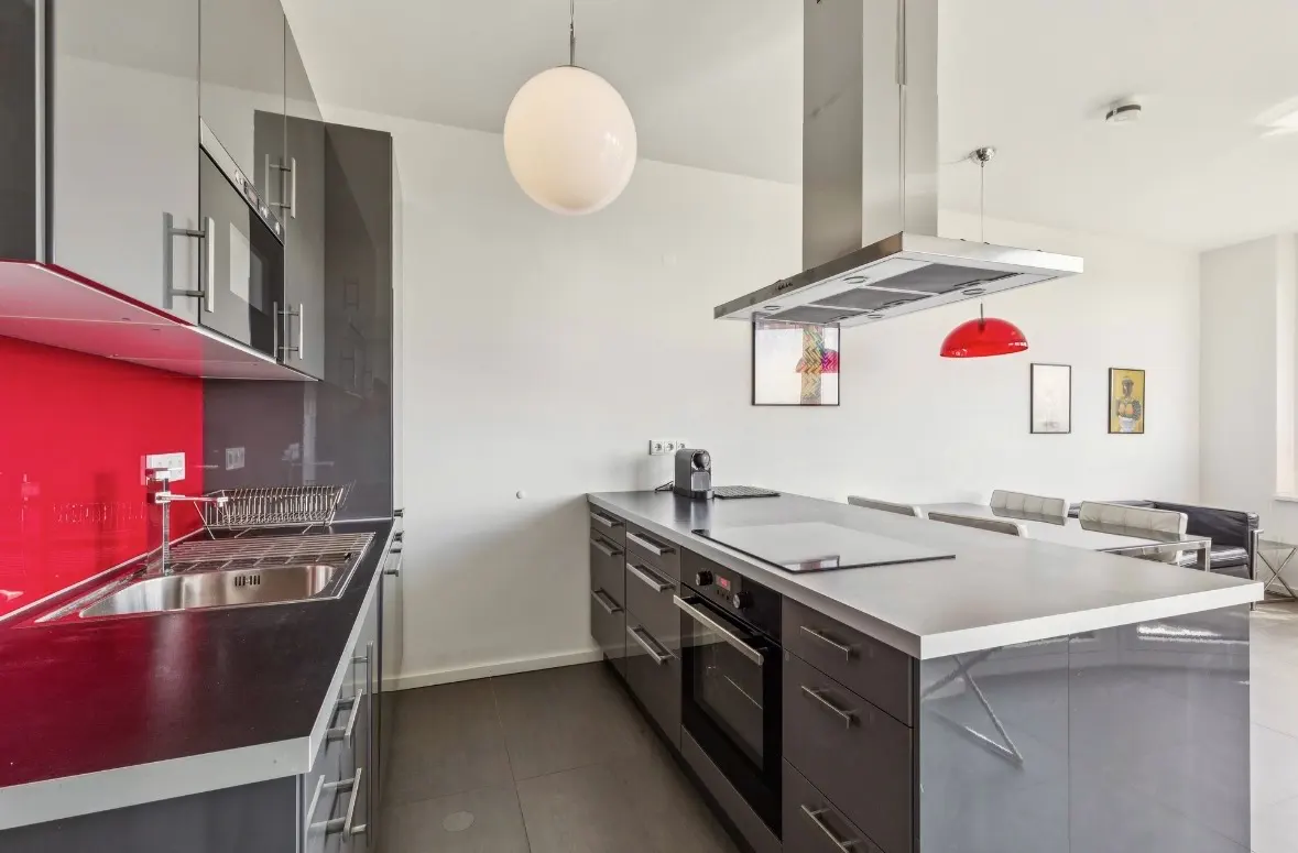 Modern kitchen with grey cabinets, a red backsplash, stainless steel appliances, and a large kitchen island.
