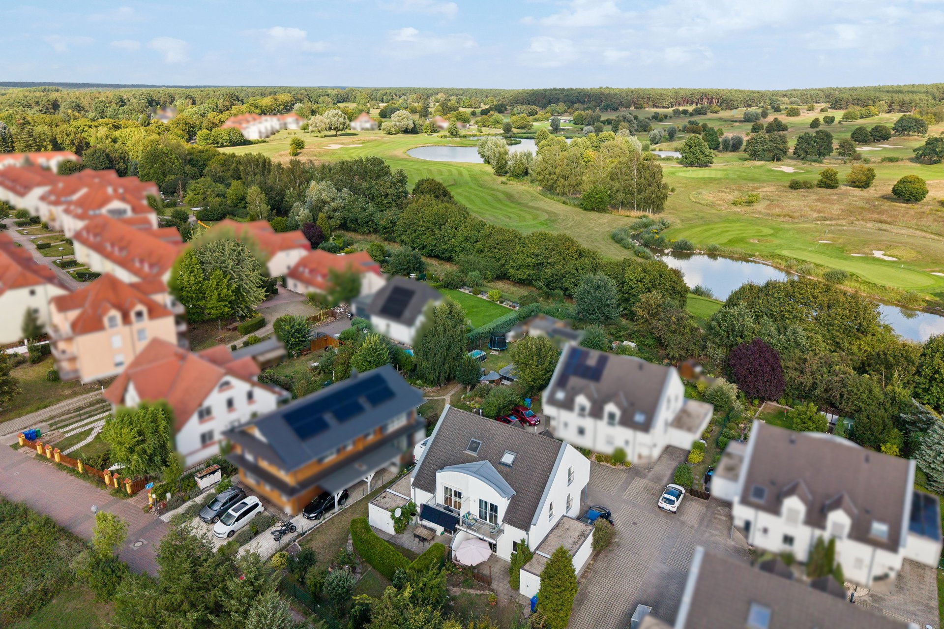 Aerial view of a residential neighborhood with houses featuring red and grey roofs, adjacent to a lush green golf course. [AI-generated text]
