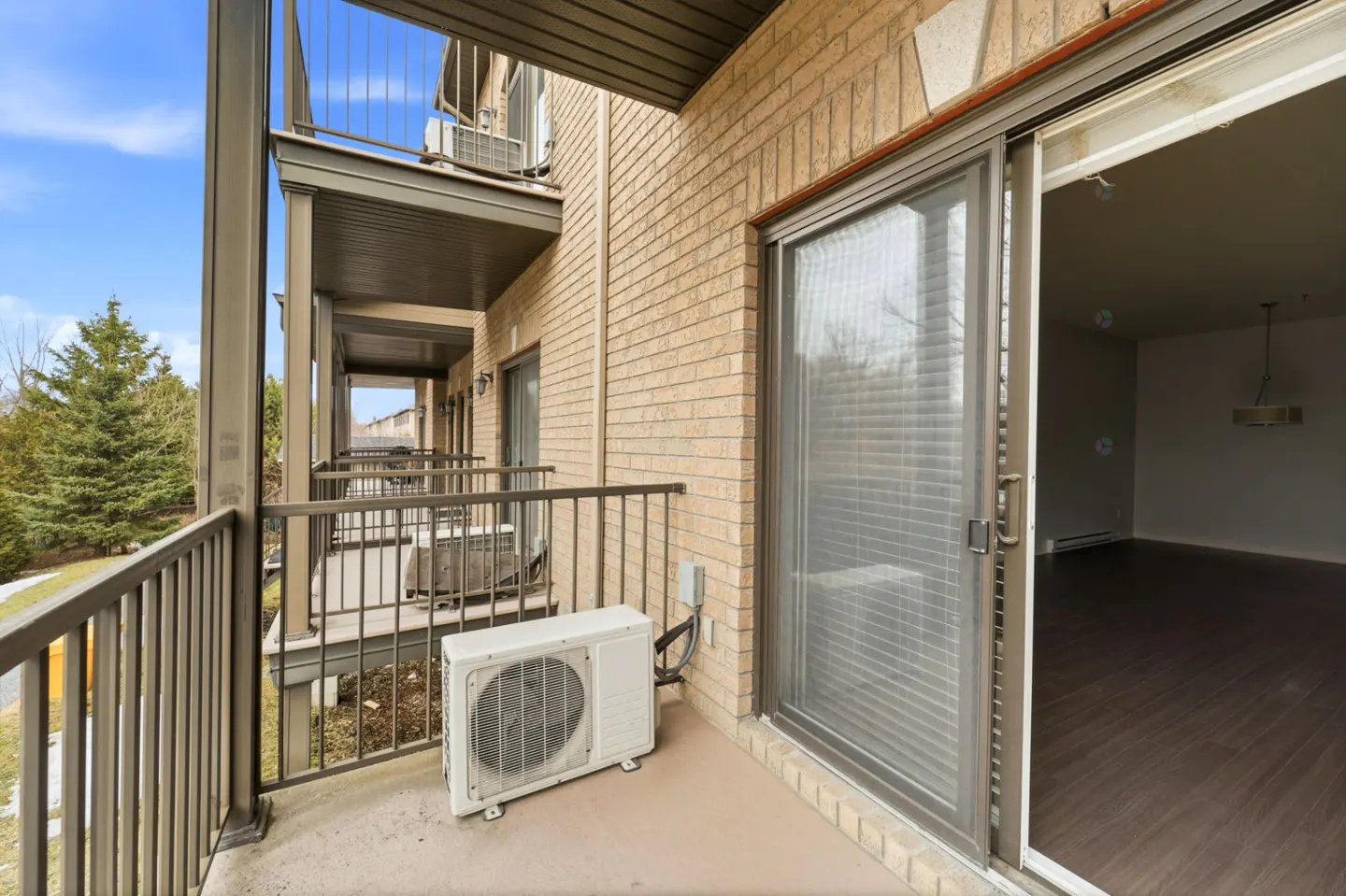 Condo balcony with metal railings, brick wall, and sliding glass door. An AC unit sits on the balcony. Interior view of the condo is visible.