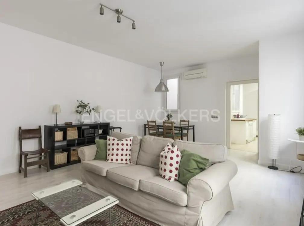Bright living room with a beige sofa, polka dot pillows, glass coffee table, and dining table in the background.