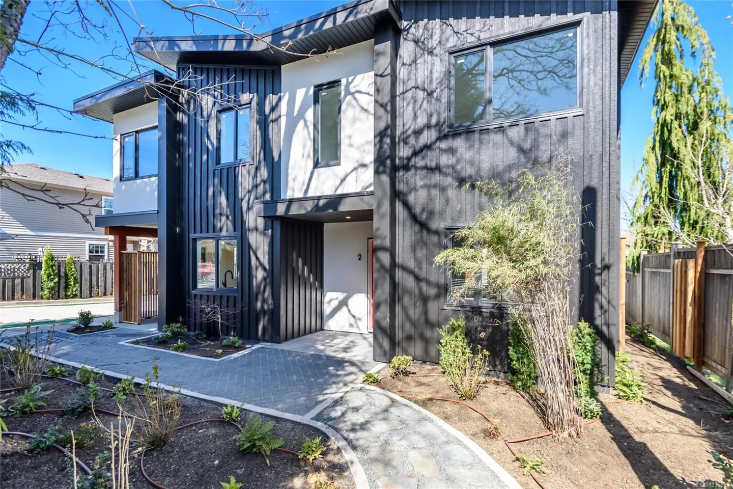 Modern two-story home with black siding and white accents. A stone walkway leads to the front door, surrounded by landscaping.