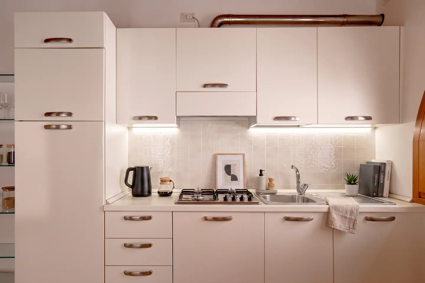 Modern kitchen with cream cabinets, stainless steel hardware, gas stove, sink, and under-cabinet lighting.