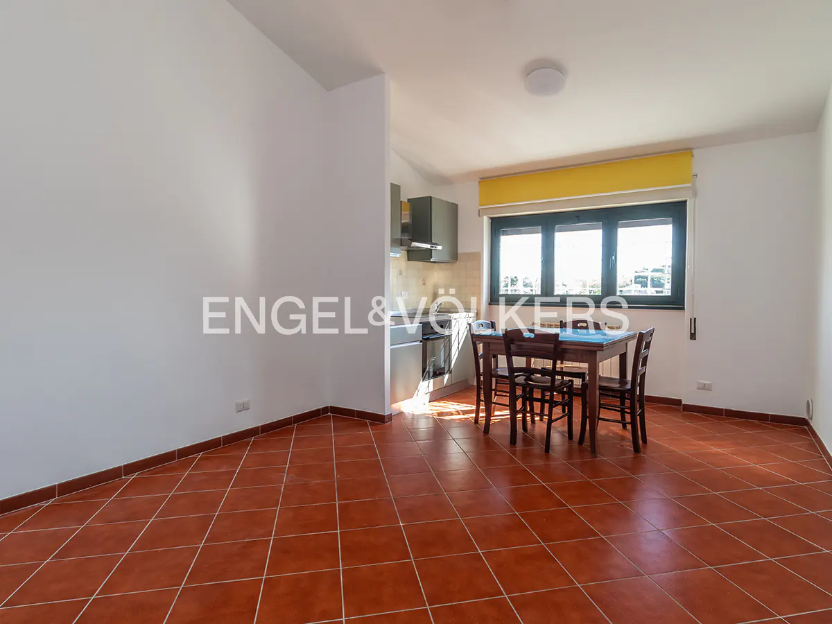 Open-plan kitchen and dining area with terracotta tile floor, white walls, and a dark wood table with chairs.