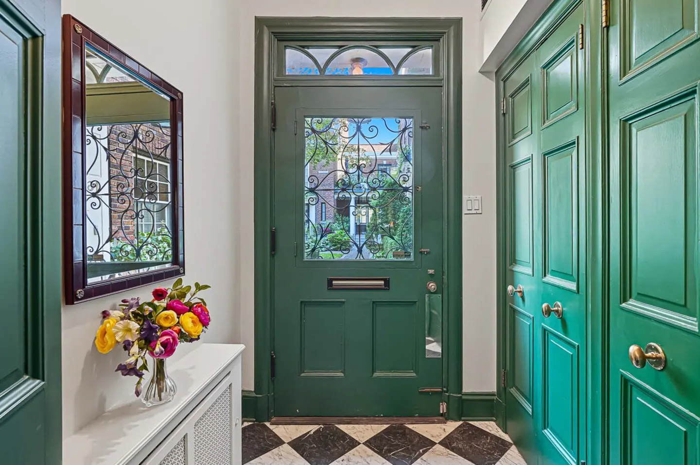 Entryway with a green front door with decorative glass, a mirror, and a bouquet of flowers on a white console table.