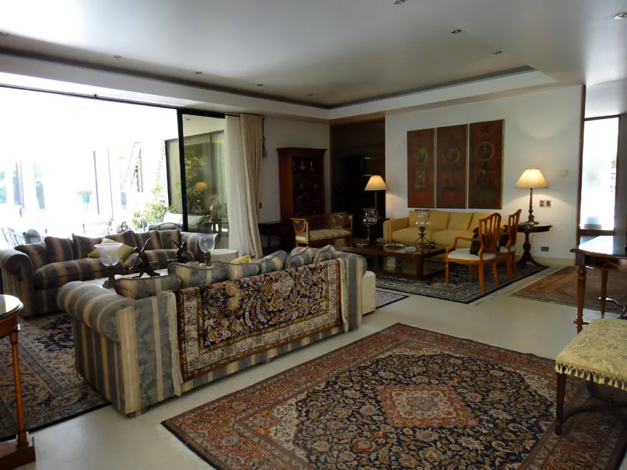 Spacious living room with striped sofas, patterned rugs, and large windows. Artwork adorns the walls, and lamps provide warm lighting.