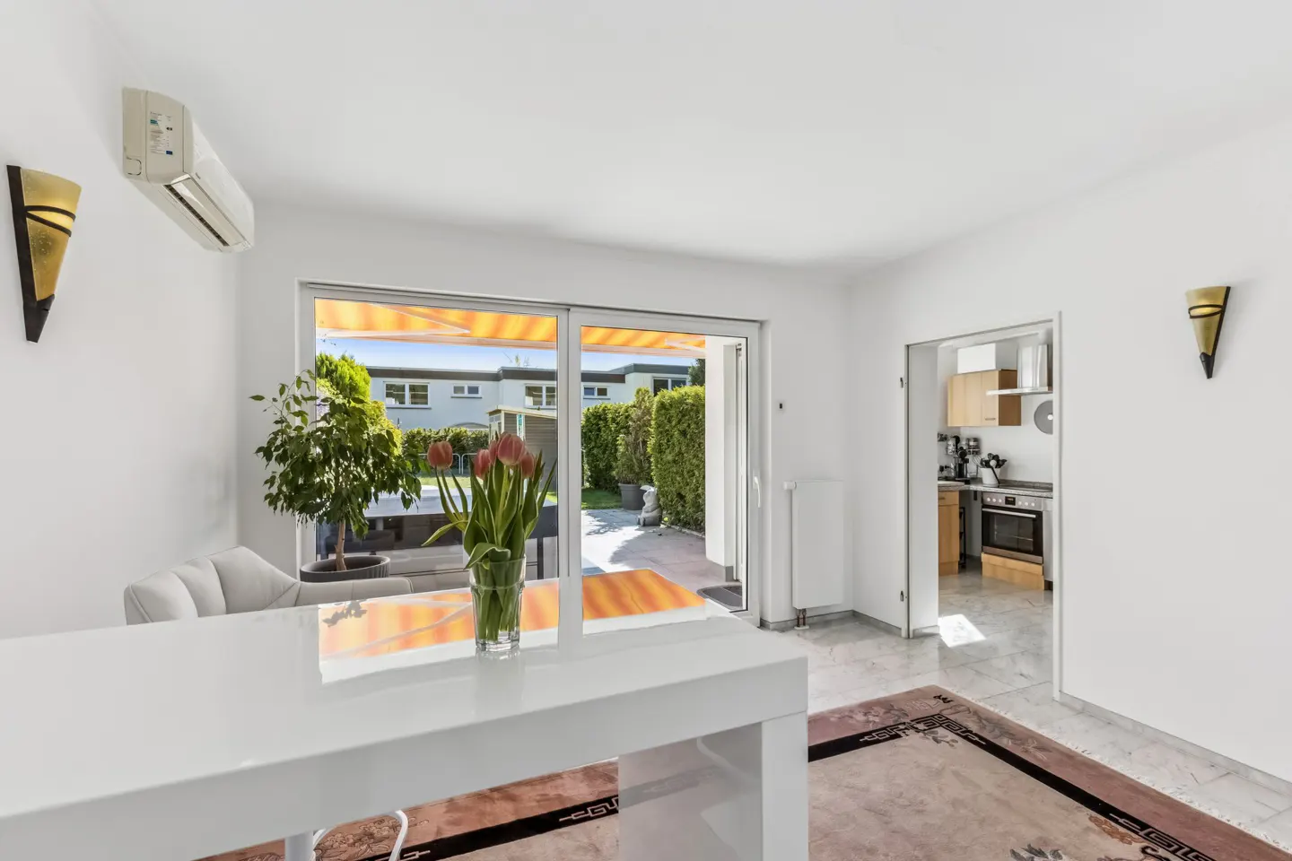 Bright, modern dining room with white walls, a white table with tulips, and a sliding glass door to a patio and garden.