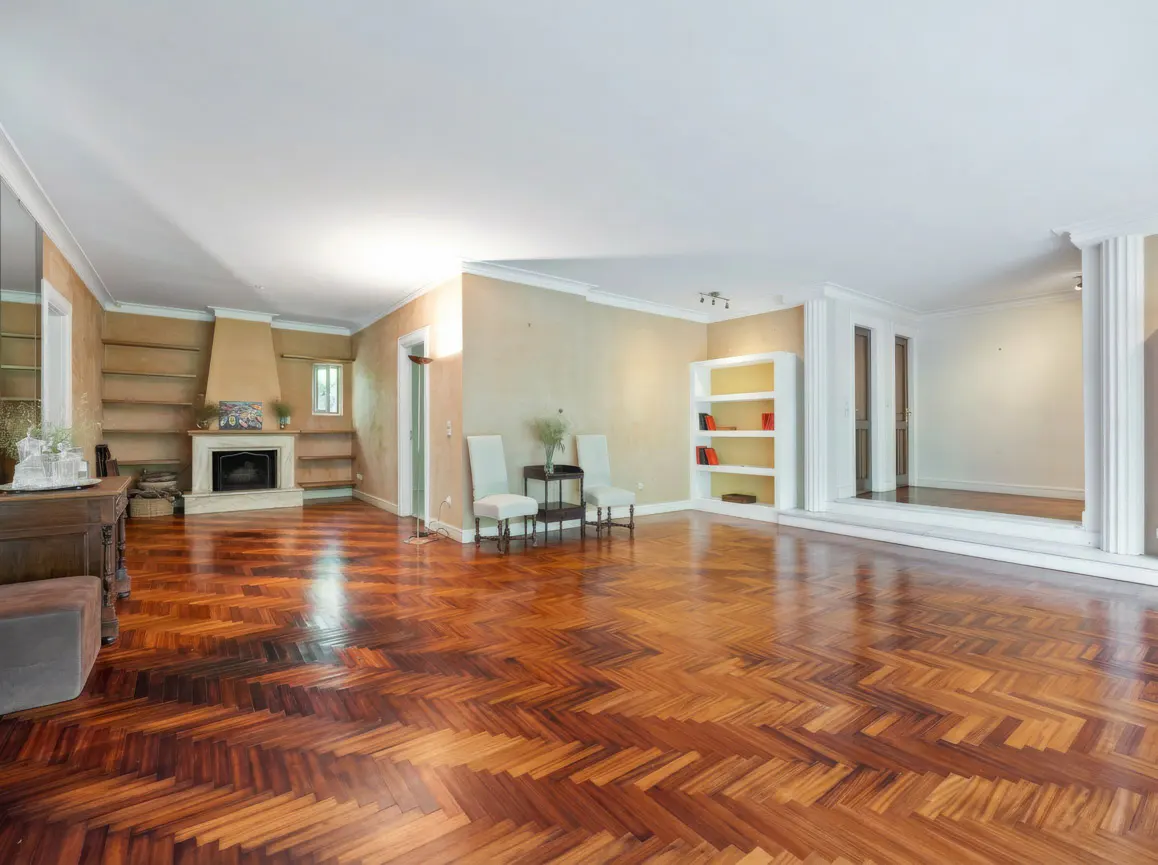Spacious living room with herringbone wood floors, fireplace, built-in shelves, and seating area. Cream walls and white trim.
