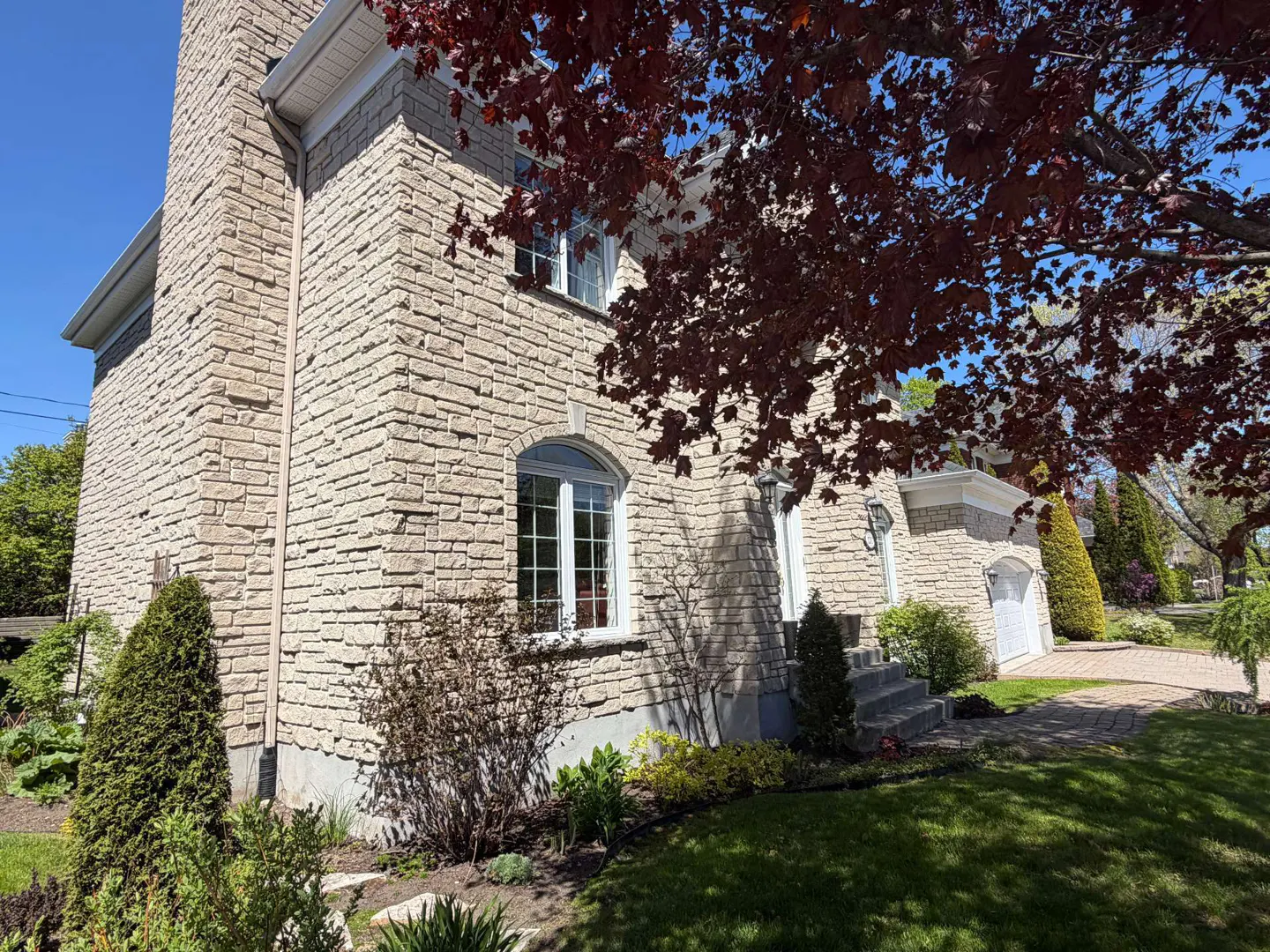 Exterior view of a two-story stone house with white trim, windows, and a red maple tree in the front yard.