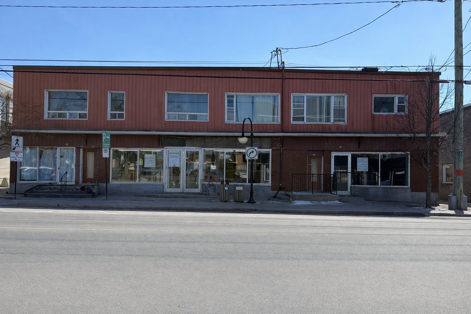 Two-story commercial building with red brick and siding, large windows, and street view.