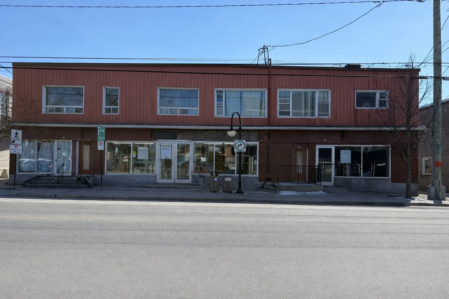 Two-story commercial building with red brick and siding, large windows, and street view.