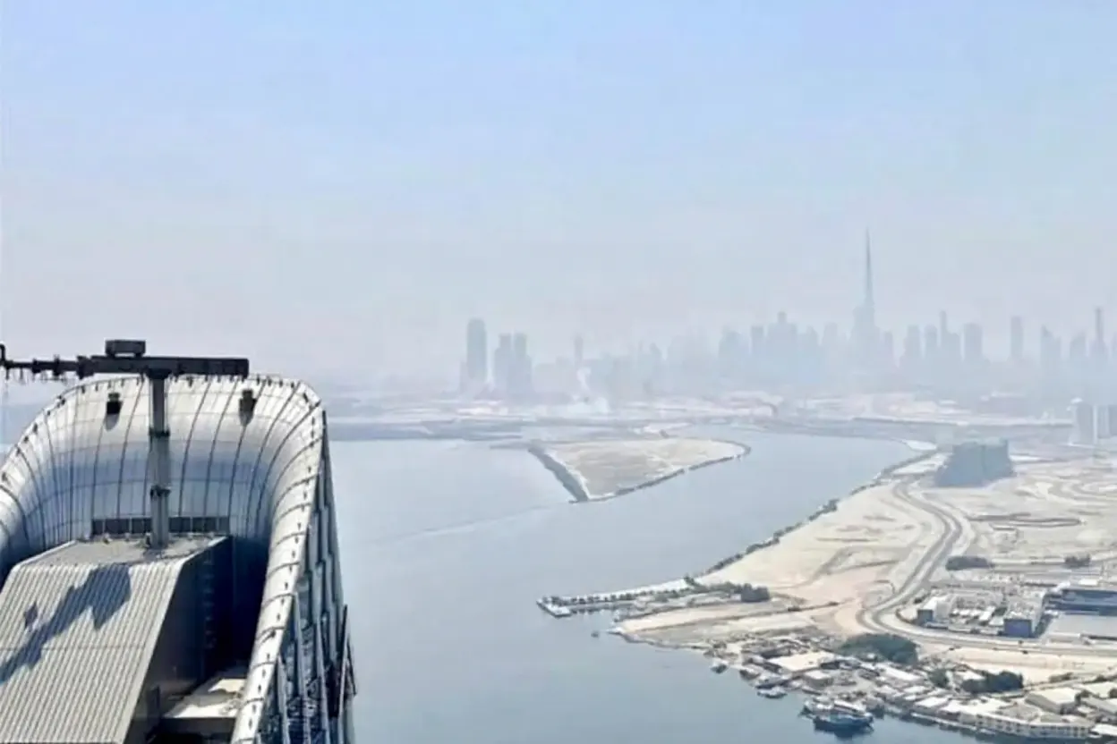 View of Dubai skyline from a building, featuring the Burj Khalifa in the distance, with water and islands in the foreground.